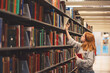 © Cavan Images - Teen girl with red hair picking a book at the library.