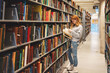 © Cavan Images - Teen girl looking through books at the library.