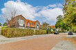 an empty street in the netherlands with houses and trees on either side, there is a car parked at the curb