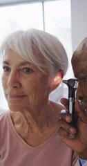 Poster - Vertical video of african american male doctor examining senior caucasian female patient at hospital