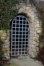 Cellar Door Formed By A Forged Lattice In The Shape Of An Arch. Sandstone Wall Of Stone Sandstone Blocks. Garden Park, Landscape, Sloping Land With Grotto