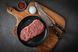 Entrecote Steak roh vom Rind mit Meersalz und roter Pfeffer auf Teller bei Vorbereitung in Küche mit Messer, Fleischgabel und Holz Brett auf Schiefer Stein Hintergrund Schwarz