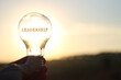Leinwandbild Motiv Hand holding light bulb with the text leadership in front of the bright sun
