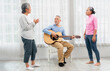 © Nassorn - Selective focus senior man happy playing acoustic guitar with friends. Elderly male musician sitting at party has fun with cheerful family singing together. Leisure activity of asian grandfather.
