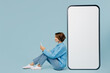 Leinwandbild Motiv Full body happy sideways young woman in knitted sweater sit near big huge blank screen mobile cell phone with workspace mockup area use smartphone isolated on plain pastel light blue cyan background