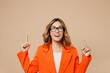 Leinwandbild Motiv Young employee business woman corporate lawyer 30s in classic formal orange suit glasses work in office point index finger overhead on worspace area mock up isolated on plain beige background studio