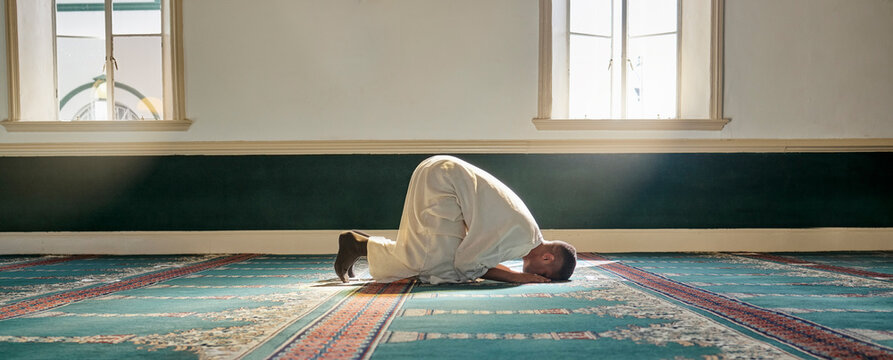 Mosque, worship and muslim man in prayer on his knees for gratitude, support or ramadan for spiritual wellness. Religion, tradition and islamic guy praying or reciting quran to allah at islam temple.