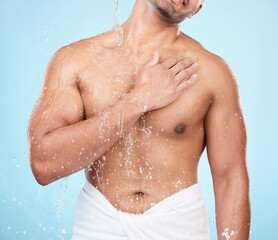 Wall Mural - Body, water and shower with a man model standing in studio on a blue background for hygiene or hydration. Splash, health and wellness with a male wearing a towel in the bathroom after bathing