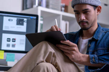 Asian male graphic designer working on tablet computer drawing sketches logo design. The concept of a new brand. Professional creative occupation with idea.