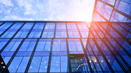 Glass modern building with blue sky background. Low angle view and architecture details. Urban abstract - windows of glass office building in  sunlight day.