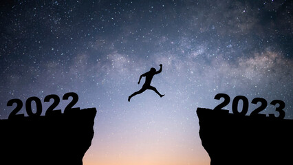 Wall Mural - Silhouette of young businessman jumping over a cliff from 2022 to 2023 with star and Milky Way over on the sky. Concept of planning, goal, challenge, new year resolution.