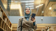 © Gorodenkoff - Portrait of Businesswoman Wearing Hijab Using Smartphone App to Share Social Media Post about Career Growth. Professional Female Manager Walking Through Office Building, Smiling and Looking Happy.