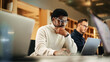 © Gorodenkoff - Portrait of Black Creative Young Man Arriving at Office for Work Office and Working on Laptop. Supervisor Smiling While Answering Email Questions From Colleagues. People Working in the Background