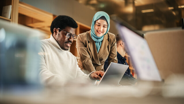 Fototapete - Two Coworkers Talking and Congratulating Eachother with a High Five. Muslim Female Chief Strategist Motivating Black Male Colleague, Showing Corporate Growth Charts on Laptop.