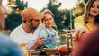 © Gorodenkoff - Portrait of a Handsome Young Father Holding His Cute Little Daughter on Lap at a Outdoors Dinner Party with Food and Drinks. Happy Family Having a Picnic Together with Friends.