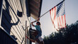 © Gorodenkoff - Proud Patriotic Dad Holding His Young Daughter of His Shoulders, Helping Her to Put the United States of America Flag on the Wall of Their House to Celebrate a National Holiday. Sunny Day in USA.