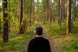 © muse studio - The guy listens to an audiobook and calm relax music in wireless headphones, stands with his back looking at nature in the forest.