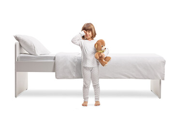 Poster - Girl in pajamas holding a teddy bear and rubbing eyes in front of a bed