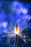 Fototapeta Na sufit - burning flickering sparkler new year fire on the background of blue lights bokeh