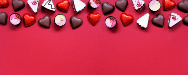 Valentines Day chocolate top border. Red and pink heart theme. Overhead view on a red paper banner background with copy space.