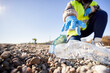 © CarlosBarquero - Group of cleanup volunteers cleaning up waste in nature and holding a garbage bag trash. Close up of activist hand picking up a plastic bottle. Concept of environmental protection.
