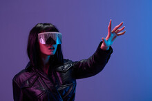 Confused Pretty Awesome Brunet Lady In Leather Jacket Trendy Specular Sunglasses Touch Invisible Object Posing Isolated In Blue Violet Color Light Background. Neon Party Cyberpunk Concept. Copy Space