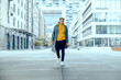 cool tough and handsome guy walk alone in city under skyscraper with grey coat and yellow sweater while being powerful and show fashion outfit in city life on street