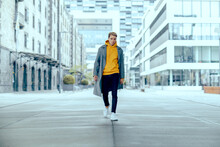 Cool Tough And Handsome Guy Walk Alone In City Under Skyscraper With Grey Coat And Yellow Sweater While Being Powerful And Show Fashion Outfit In City Life On Street