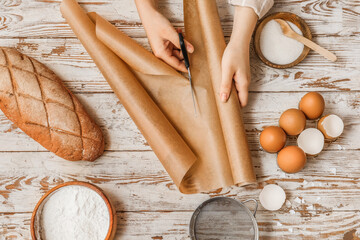 Woman cutting baking paper on white wooden background, top view