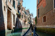 View from gondola with narrow canal of water surrounded by old buildings on sunny day in Venice, Italy.