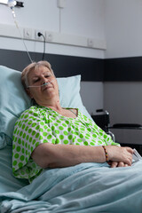 Wall Mural - Old lady resting on bed at hospital room. Elderly woman sedated for surgery in clinic. Senior female resting, sleeping, recovering from infection. Patient with disease using medical aid for breathing.