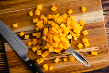 Canvas Print - Butternut Squash Cut Into Small Cubes on a Wood Cutting Board: Diced winter squash on a wooden background with a kitchen knife