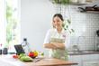 © David - Portrait of attractive asian japanese woman in kitchen at home, young girl browsing website on tutor cooking class and doing for kitchen, cutting vegetables, cooking, cooking concept.