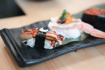 Wall Mural - Selective focus on foie gras sushi with a blur of other sushi on the rectangular black ceramic plate.