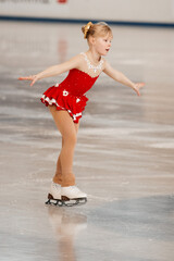 Wall Mural - a little girl in a red dress participates in a figure skating competition	