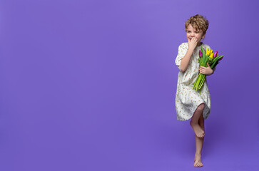 Cute caucasian laughing preschool girl standing over purple background, hold bouquet of yellow tulips. Copy space for advertisement. Spring freshness positive shopping educational concept