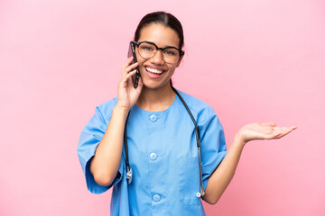 Wall Mural - Young nurse Colombian woman isolated on pink background keeping a conversation with the mobile phone with someone