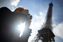 Low Angle View Of Man Photographing Through DSLR Camera Against Eiffel Tower During Sunny Day