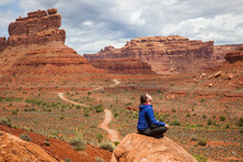 A Woman Sits On A Boulder In The Valley Of The Gods, Utah.