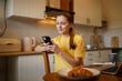 © Daryna  - A young attractive woman in a yellow t-shirt is holding a phone and typing while sitting on a chair in her kitchen. A place for remote work and online communication