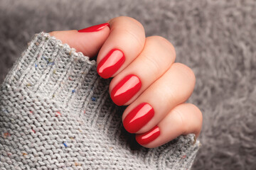 Wall Mural - Female hand with beautiful manicure - red nails on gray fluffy knitted fabric. Nail care concept