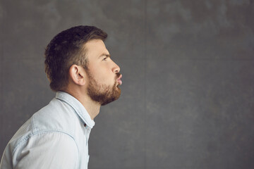 Profile view of young man in love pouting lips giving big smooch or throwing air kiss at empty side. Funny casanova lady killer womanizer guy eyes open pretending to make out with imaginary girlfriend