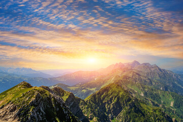 Wall Mural - Panorama of a mountain range with alpine meadows during sunset with beautiful sky cloudscape.