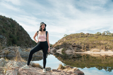 young latin woman hiking standing on a rock on a lake in the middle of two mountains