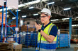 © supAVADEE BUTRADEE - Asian male workers wearing reflective jackets and safety helmets use walkie-talkiescommunicating with colleagues inside warehouse distribution center to deliver supplies.Factory and logistics concept.