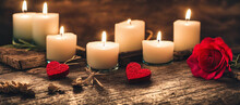 Romantic Scene With Bunch Warm Glowing Candles And Two Heart Shaped Felt And Red Rose Laying At Old Wooden Table With Some Fog Steam In Air, Generative AI