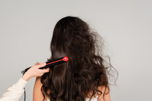 Hairdresser Straightening Hair Of Curly Brunette Woman With Hair Iron Isolated On Grey.