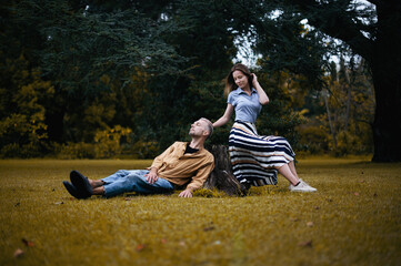 A romantic photo of a young couple in a beautiful autumn park, with the woman sitting on a tree stump and the man lying nearby