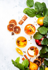 Wall Mural - Hot Mulled Cider glass cups: apple, pear and orange ciders with spices. Fermented low alcohol winter fruit drink on white table with leaves, top view