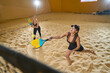 Two women are on field for playing beach tennis indoors
